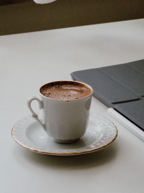 Free A white cup of hot coffee with a saucer and a notebook on a table. Stock Photo