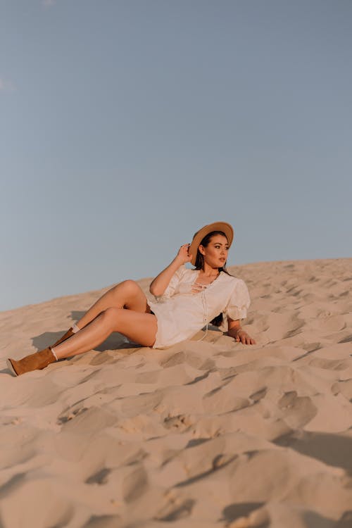 Free Woman in White Dress Lying on Brown Sand Stock Photo