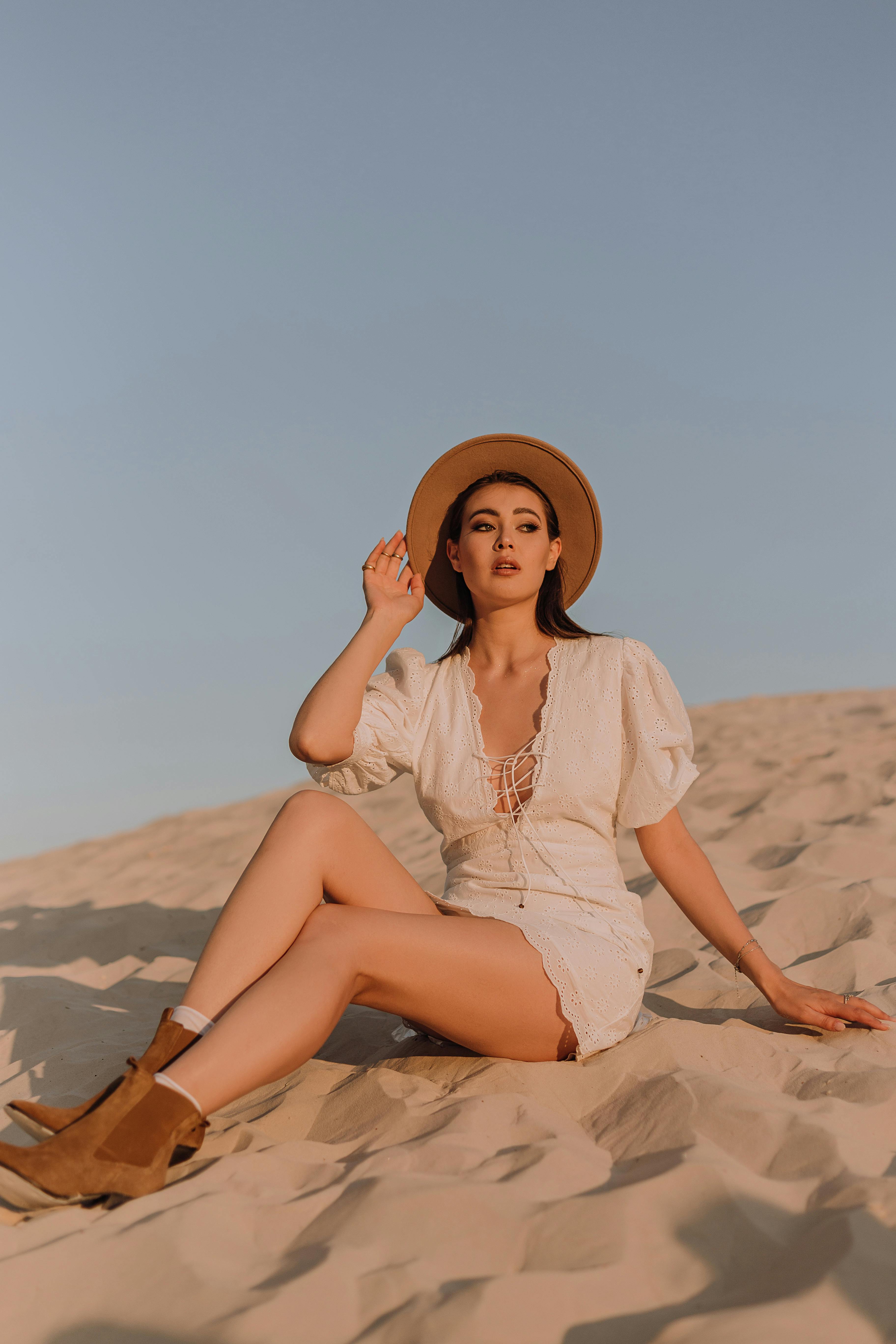 Woman in White Dress and Hat Sitting in Desert  Free Stock Photo