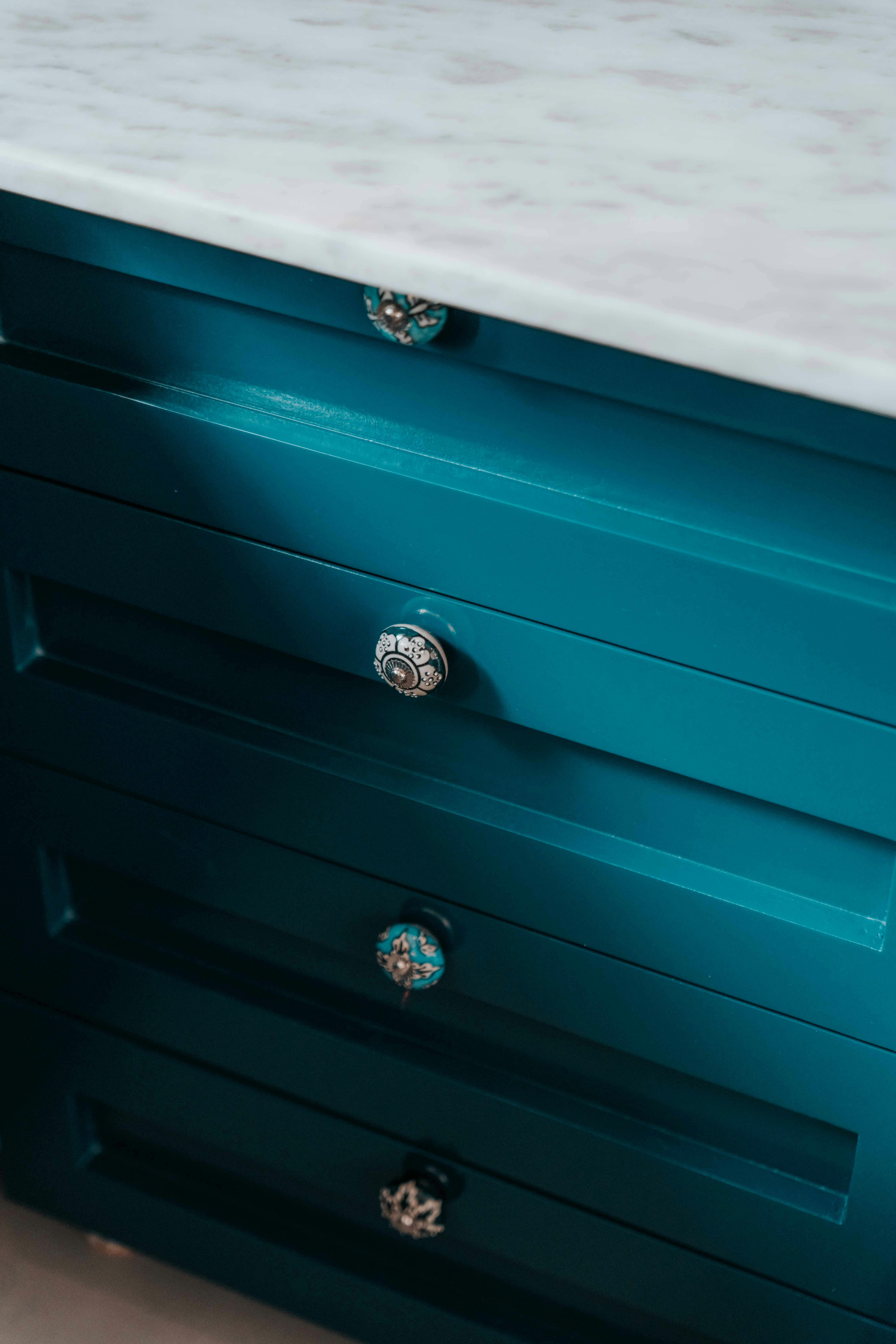 A stylish blue cabinet highlighting its ornate knobs and marble top.