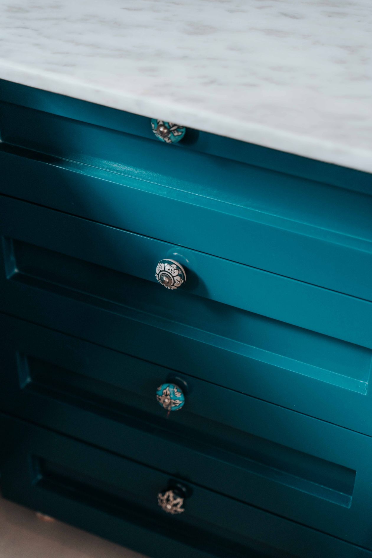 Blue cabinet with ornate knobs under a marble countertop