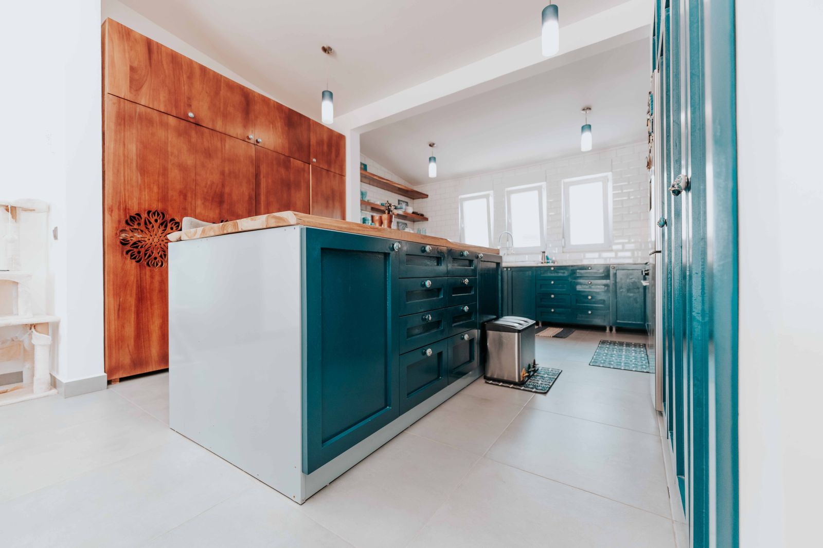 Deep blue-green kitchen cabinet fronts beside wood cabinetry and counters in a light room.