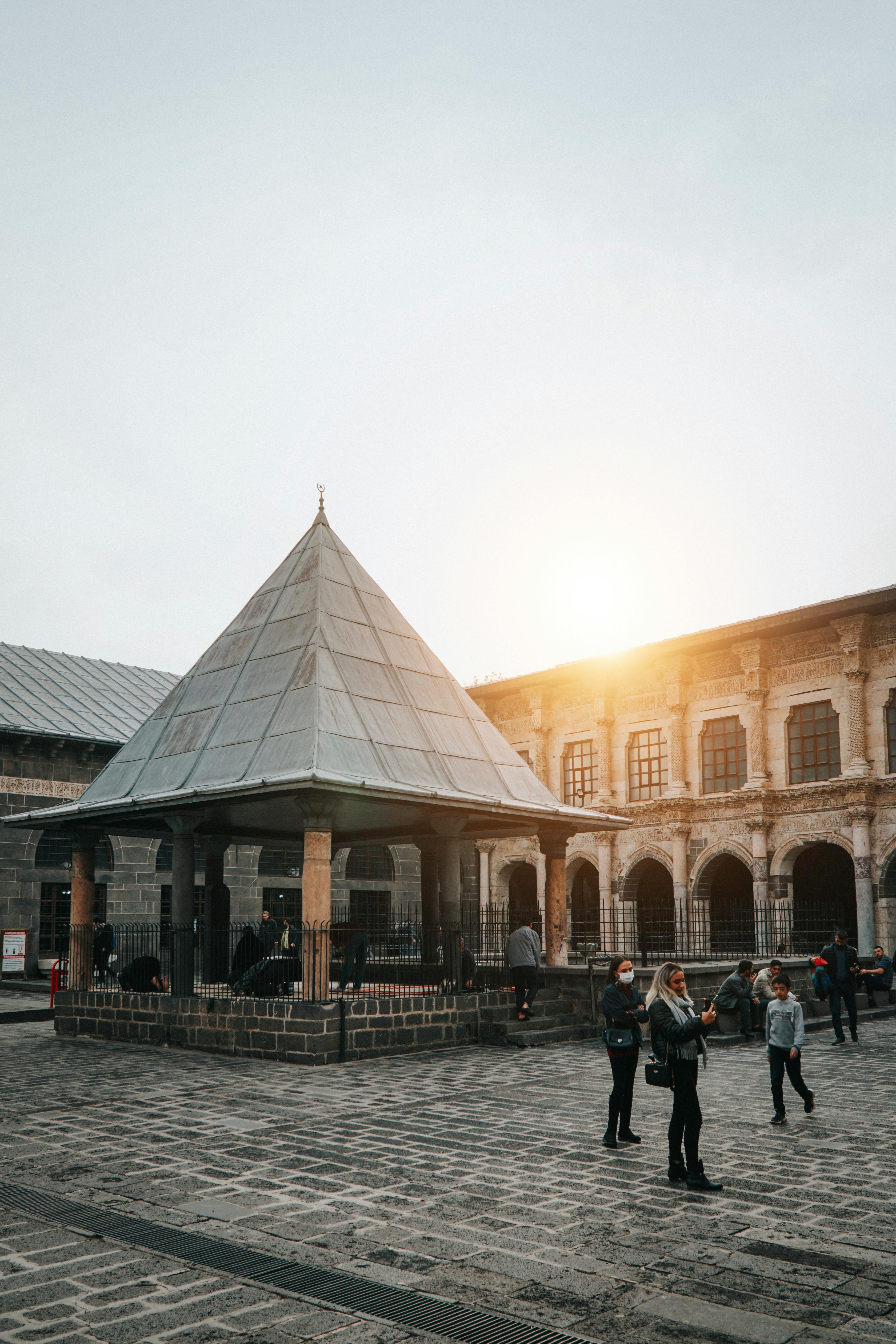 A scenic view of a historic courtyard in Diyarbakır, Turkey, featuring ancient architecture and people at sunset.