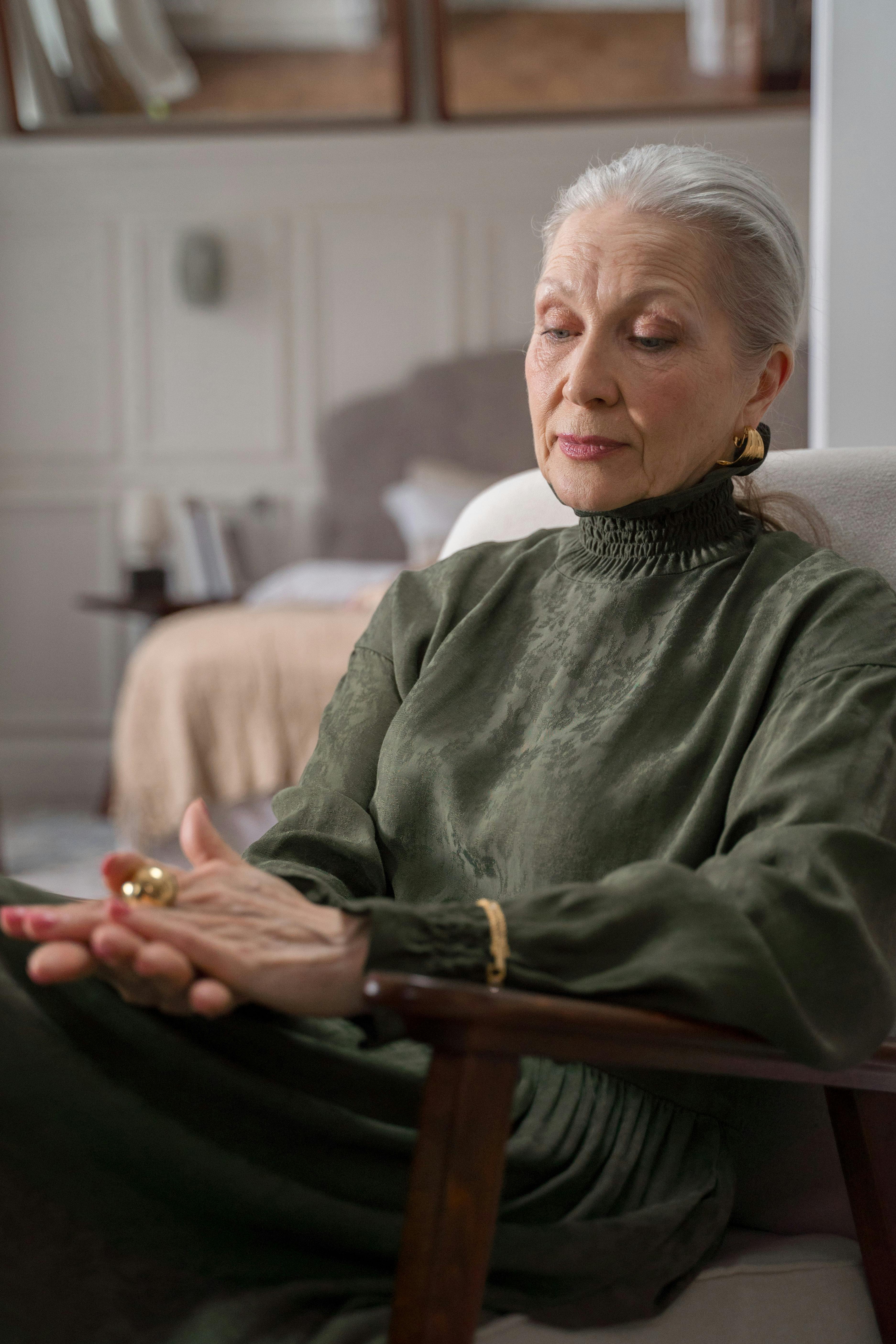 elderly woman sitting in chair and looking at her gold ring