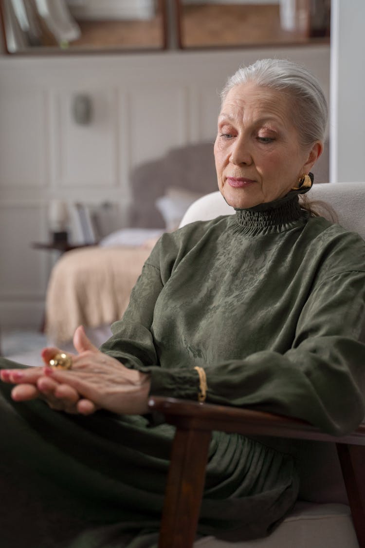 Elderly Woman Sitting In Chair And Looking At Her Gold Ring