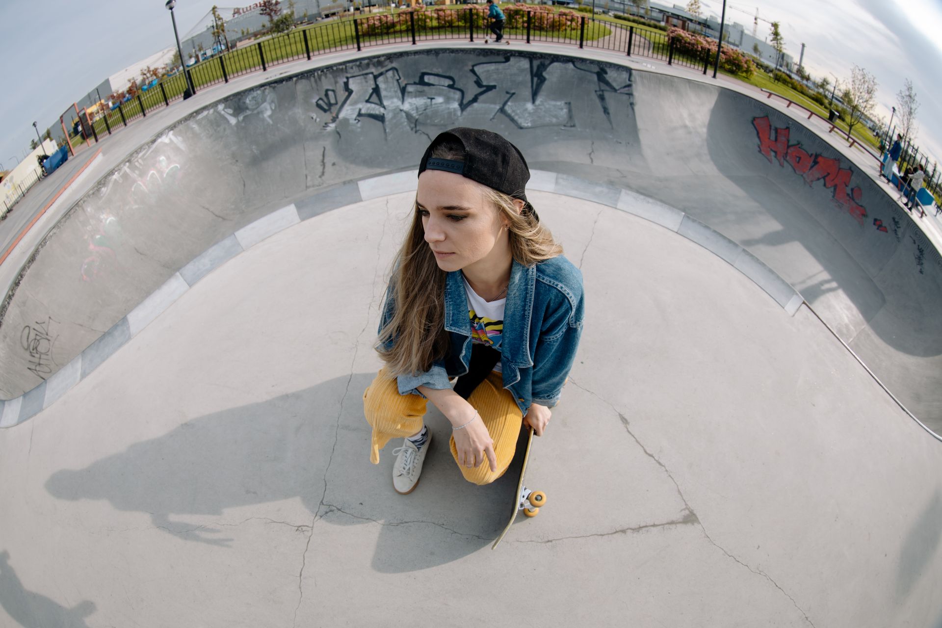 Young woman in casual attire holding skateboard at an outdoor skate park. Perfect for lifestyle and fashion content.
