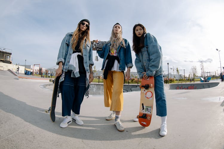 Group Of Teenage Girls Wearing Jackets Posing And Standing On Skate Park