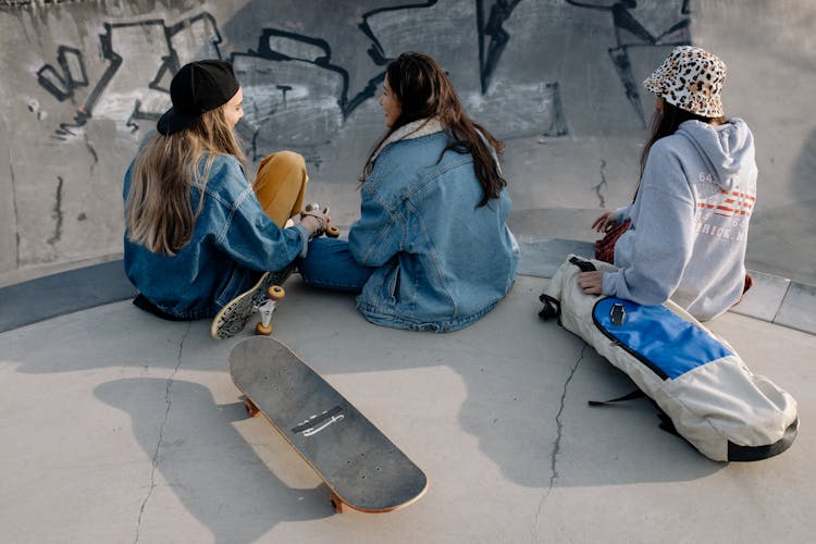 Group Of Teenage Girls Wearing Jackets Sitting On Concrete Ground