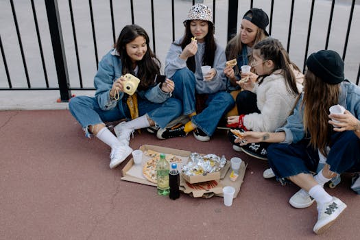 Group of young women enjoying an outdoor picnic with pizza and drinks. Casual and lively scene.