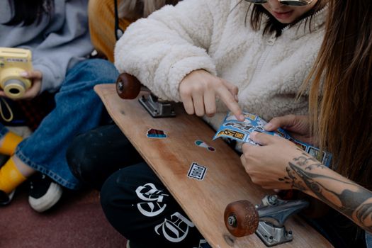 Teenagers decorate a skateboard deck with stickers, enjoying a creative outdoor activity.