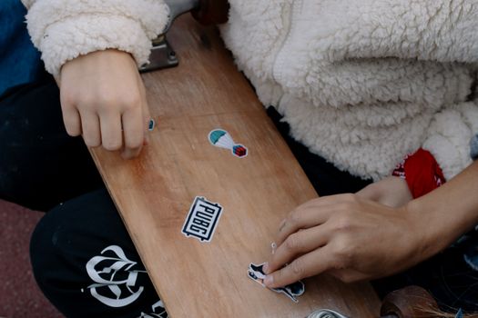 Close-up of hands placing stickers on a skateboard, showcasing creativity and personal style.
