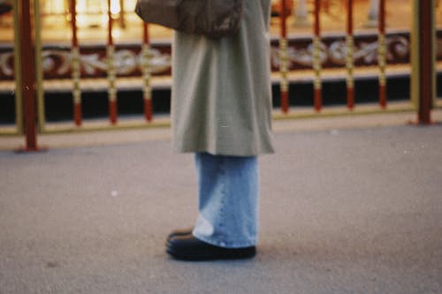 A Person Wearing a Coat and Denim Jeans Standing on the Concrete Surface