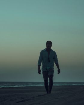 A man walks alone on a serene beach during twilight, creating a peaceful silhouette against the sea.