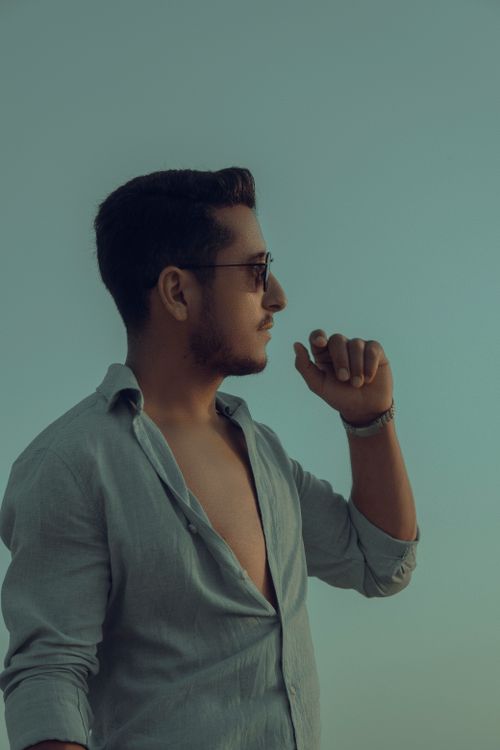 Free A young man in sunglasses and open shirt stands outdoors in profile view, looking thoughtful. Stock Photo