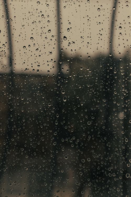 Free Raindrops on a glass window, creating a moody atmosphere with a blurred outdoor view. Stock Photo