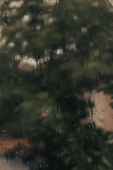 Blurred view of nature through a rain-splattered window, evoking a serene and moody atmosphere.