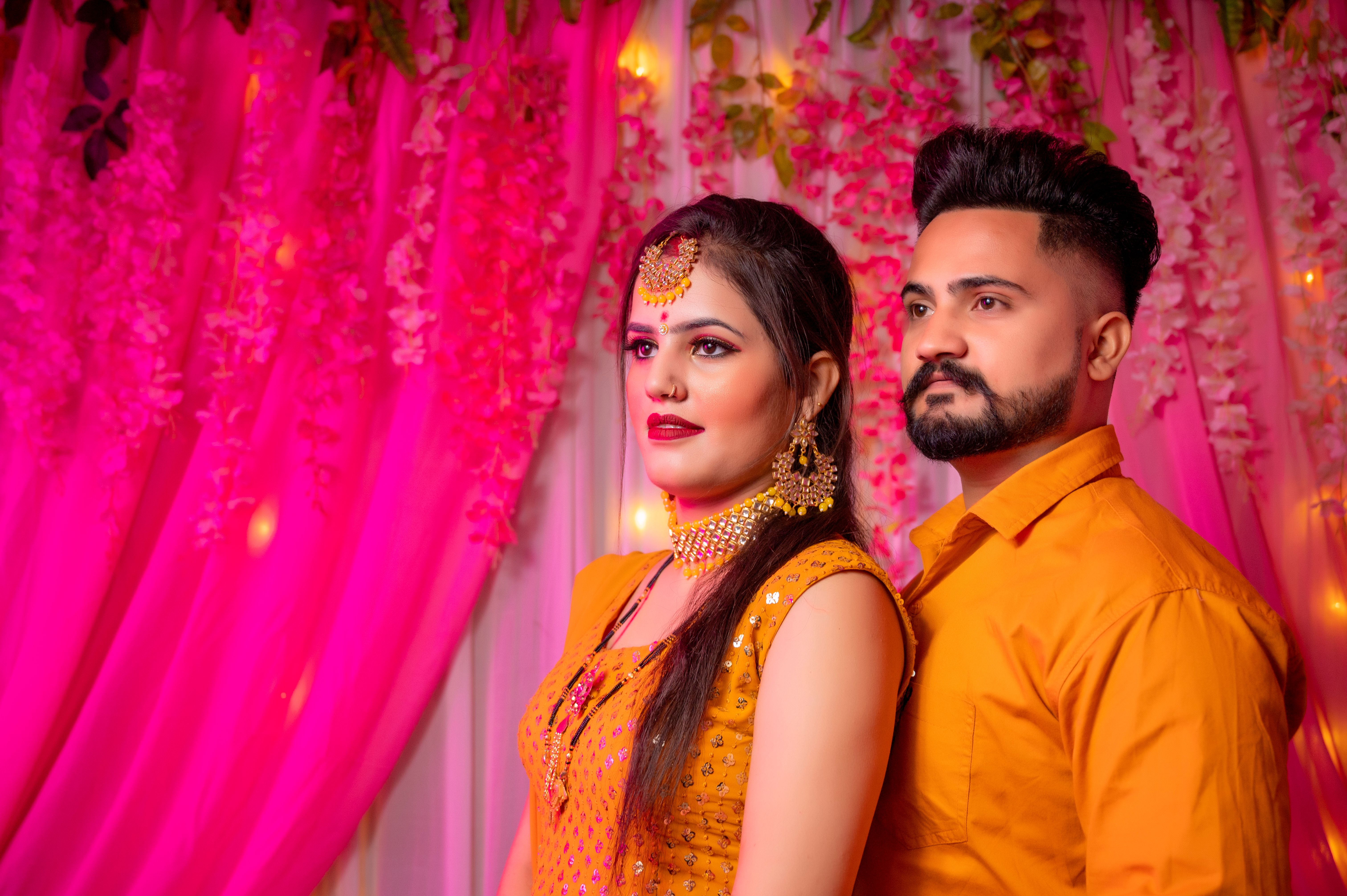 A couple poses in vibrant traditional clothing indoors surrounded by floral decor.