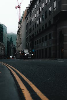 A black taxi driving down an empty urban street lined with tall buildings.