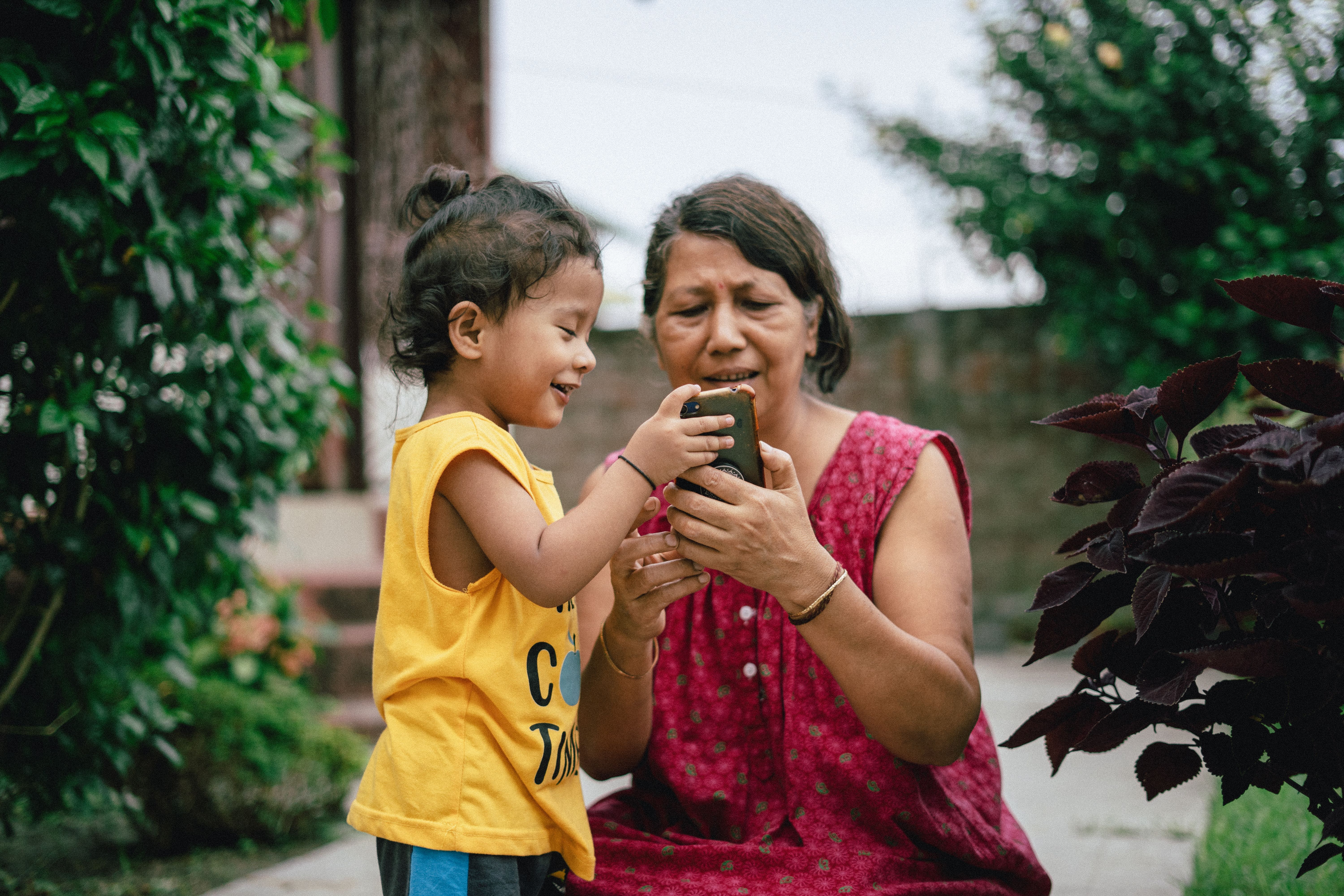 A vibrant community garden with people of all ages working together, with smartphones visible