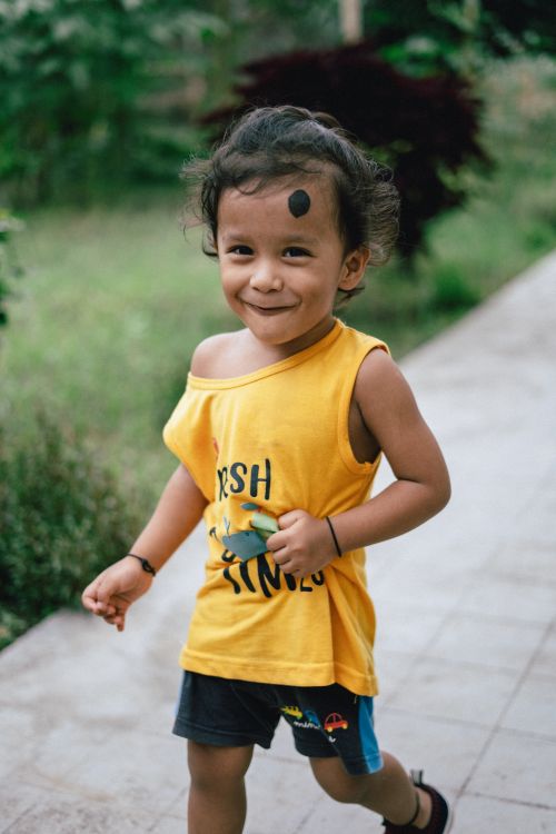 Free Happy child in yellow tank top enjoying a playful moment on a garden pathway outdoors. Stock Photo
