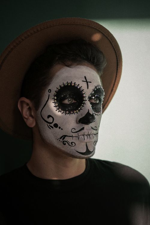 Free Close-up of a man with Day of the Dead face paint and a hat, reflecting cultural celebration. Stock Photo