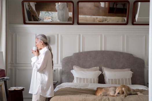 Senior woman sipping coffee by the bed with her dog in an elegant bedroom setting.