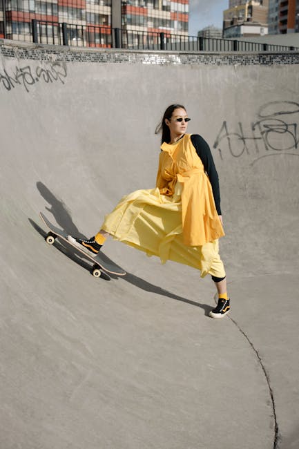A stylish woman in a yellow dress and sunglasses skates on a bowl ramp in a city skatepark.