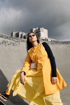 A fashionable young woman posing confidently in a skate park wearing a striking yellow dress.