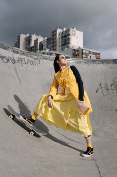 Fashionable woman in yellow dress posing with skateboard outdoors.