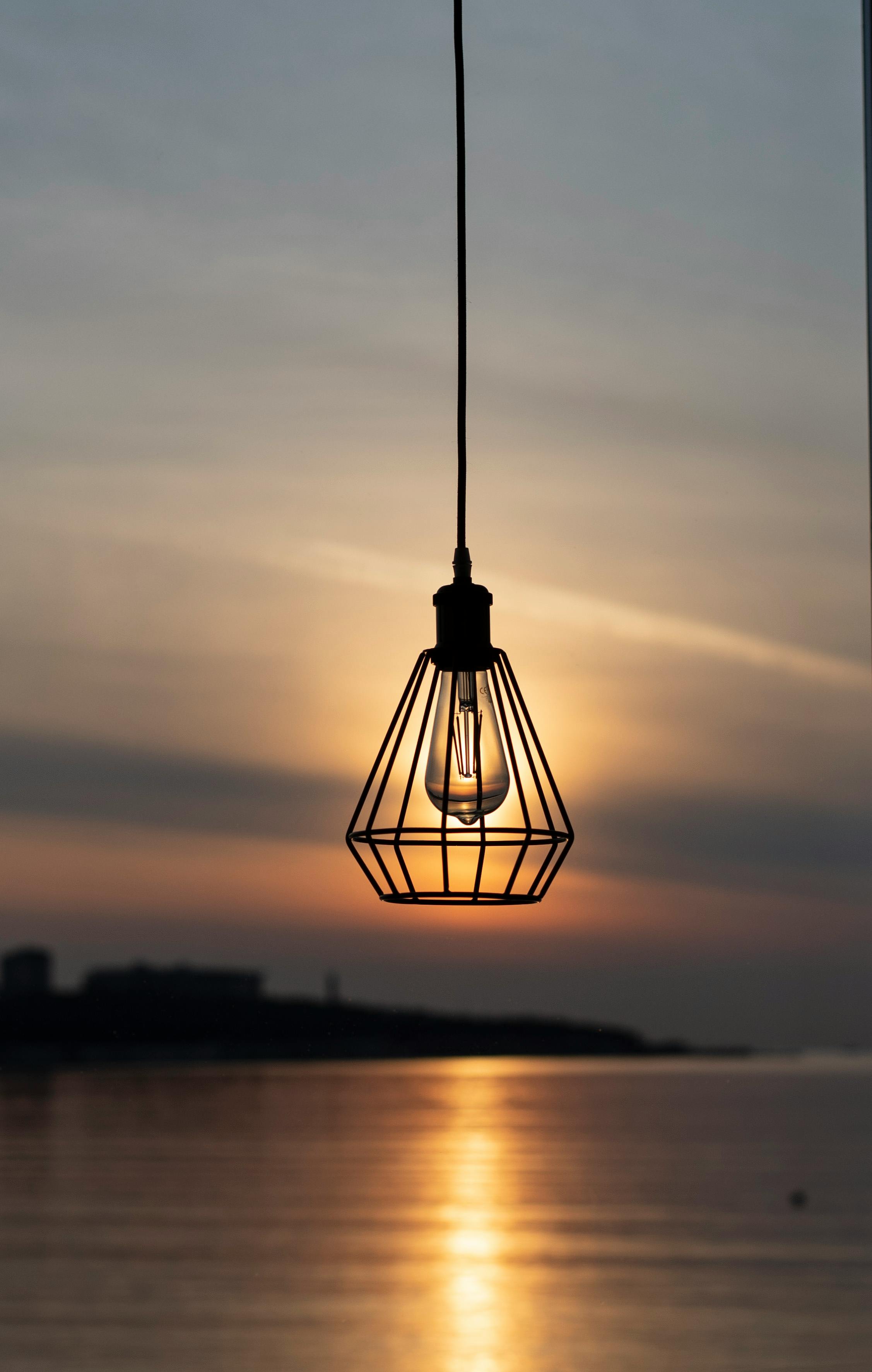 Silhouette of a hanging light bulb against a beautiful sunset over water.