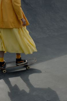 A fashionable person rides a skateboard at a skatepark wearing a vibrant yellow dress, showcasing style and athleticism.