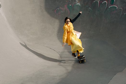 Stylish woman in yellow outfit skateboarding in an urban skatepark, showcasing modern fashion and urban lifestyle.