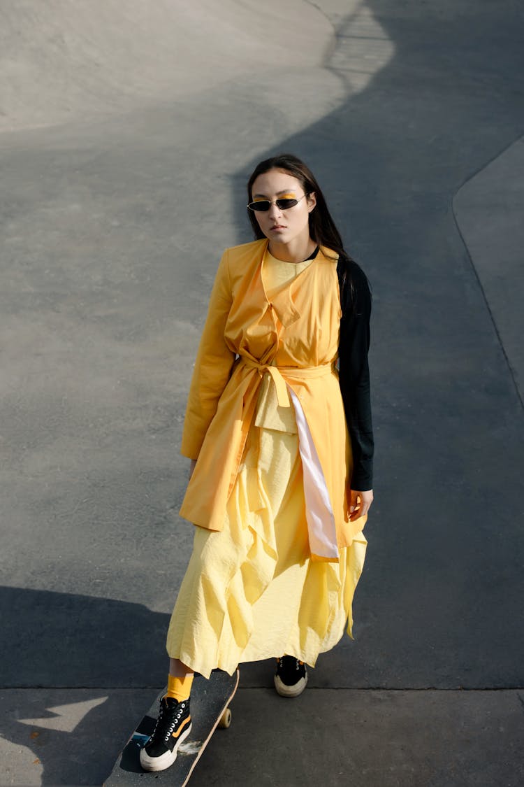 A Fashionable Woman In Yellow Dress Skateboarding