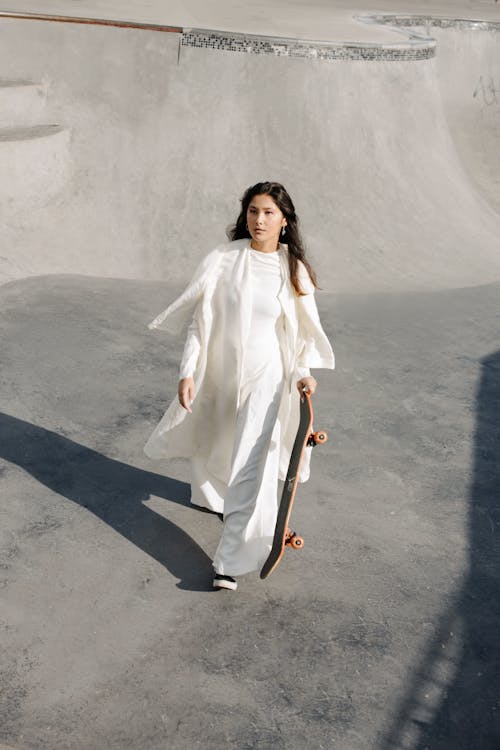 Woman Walking in White Long Dress Holding a Skateboard