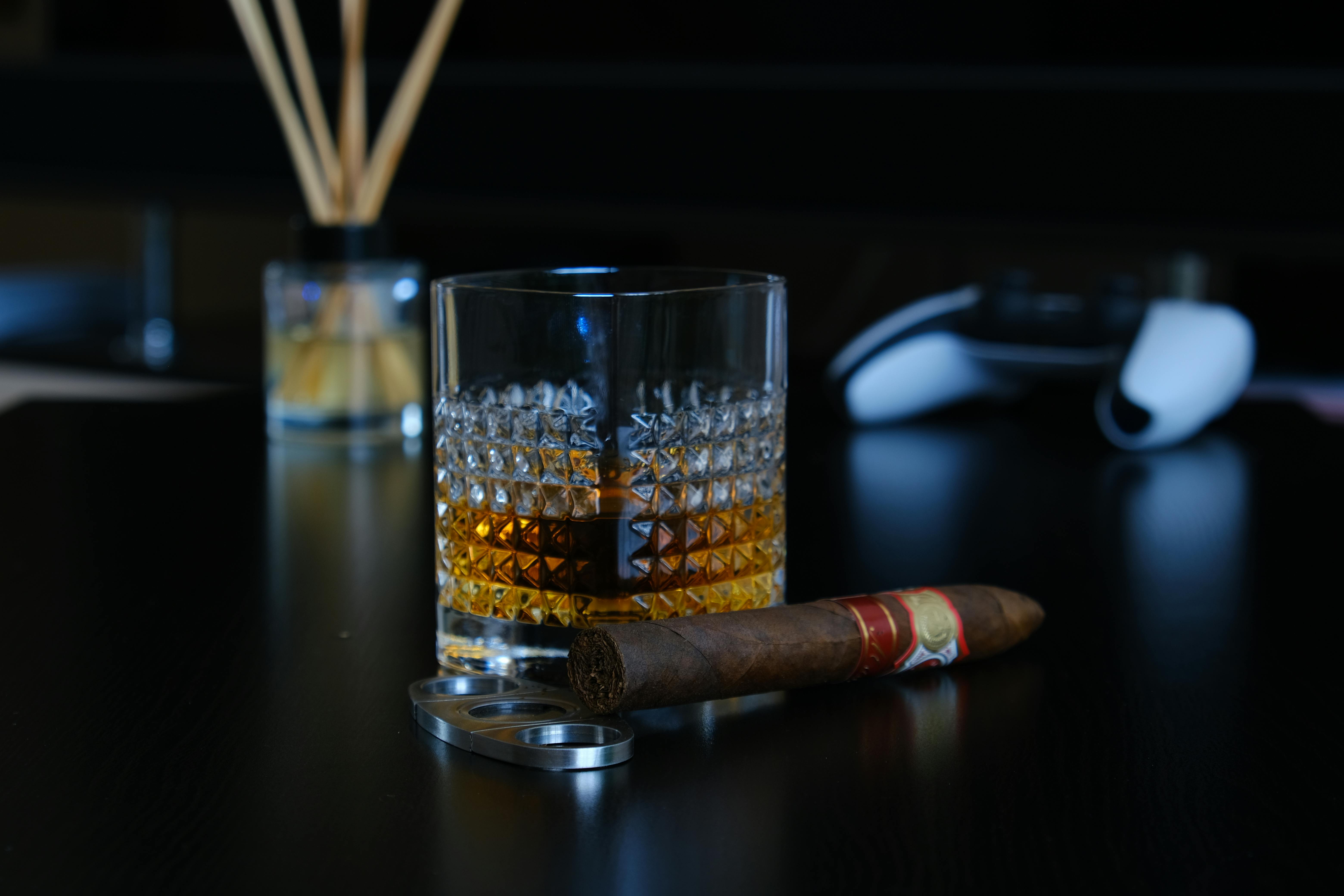 A glass of whisky with a cigar on a dark tabletop, embodying luxury and relaxation.