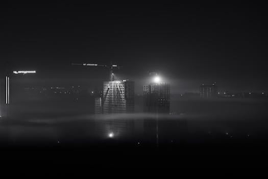 A foggy night view of Moscow's modern skyline with illuminated buildings and construction cranes.