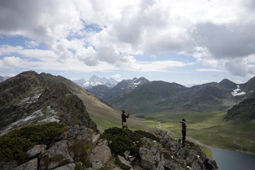 A Person Taking Picture of a Person Standing Near the Edge of a Rocky Mountain