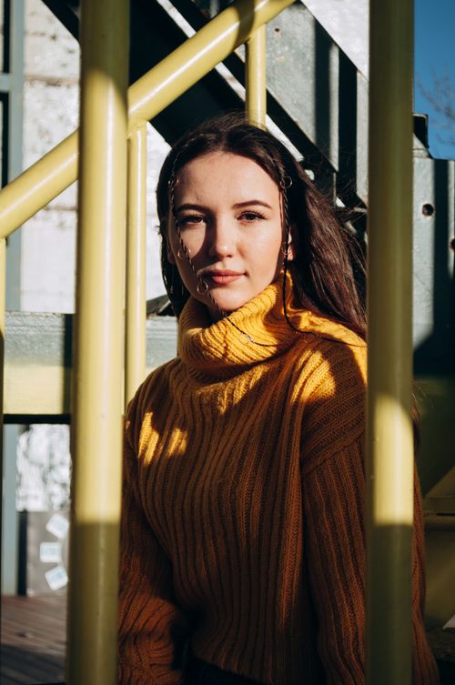 Free Portrait of a woman in a yellow sweater sitting on a sunlit staircase outdoors. Stock Photo