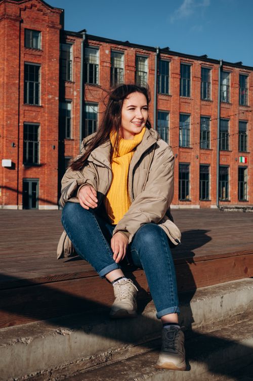 Free Casual and cheerful young woman sitting and smiling on urban steps in sunlight. Stock Photo