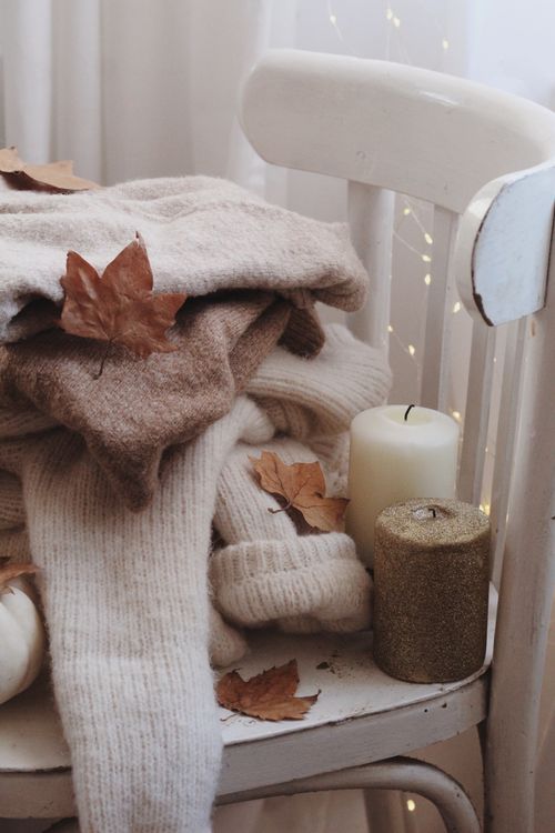 Free Warm fall setting with sweaters on a chair, candles, and leaves for autumn ambiance. Stock Photo