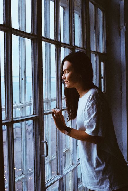 A thoughtful woman gazes out a window in Saint Petersburg, capturing a serene indoor moment.