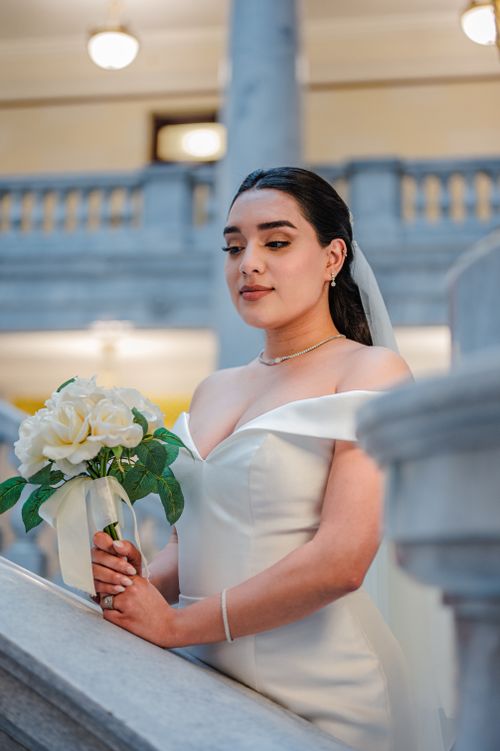 Free A bride in a stunning white wedding dress holds a bouquet of flowers indoors with graceful elegance. Stock Photo