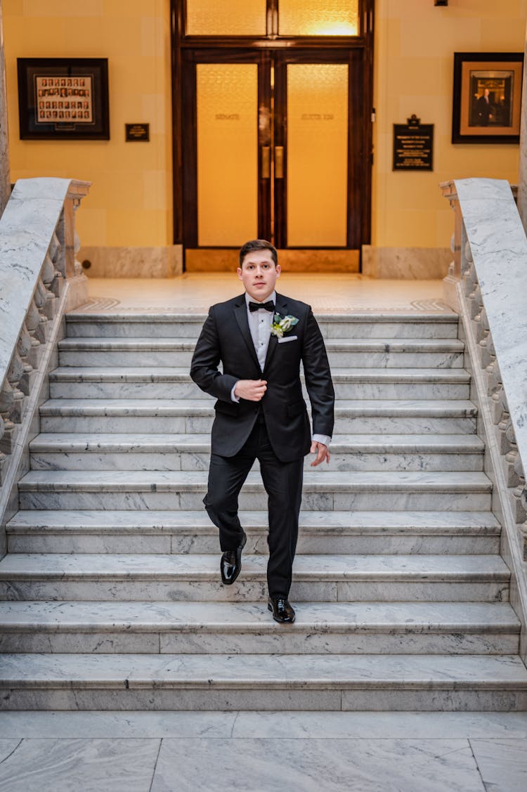 A Bridegroom Walking Down Marble Stairs Wearing Wedding Suite And Looking At Camera 