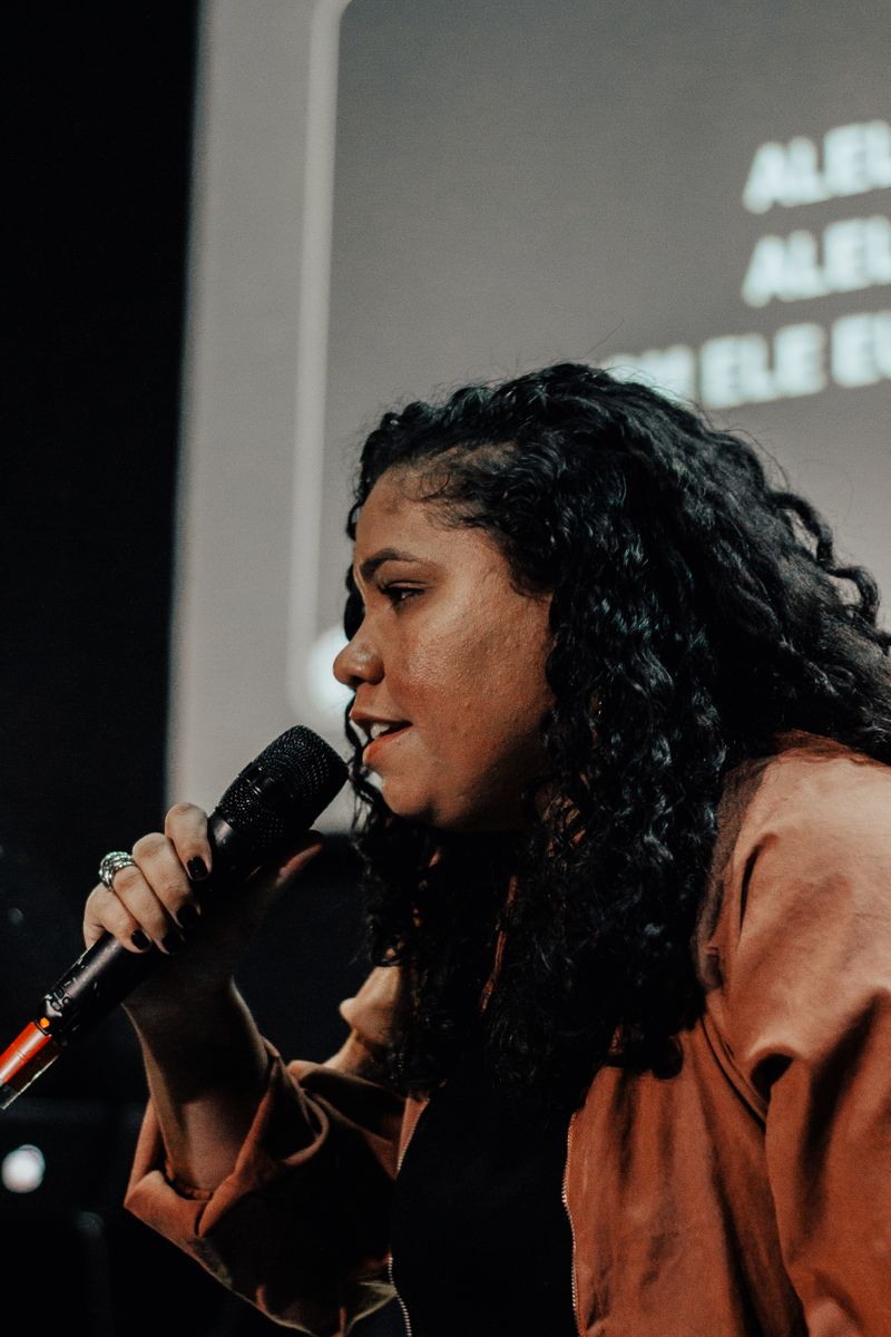 A speaker on a darkened stage, microphone in hand — photo by Igreja Dimensão on Pexels