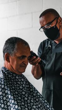 A senior man receiving a haircut from a masked barber indoors.