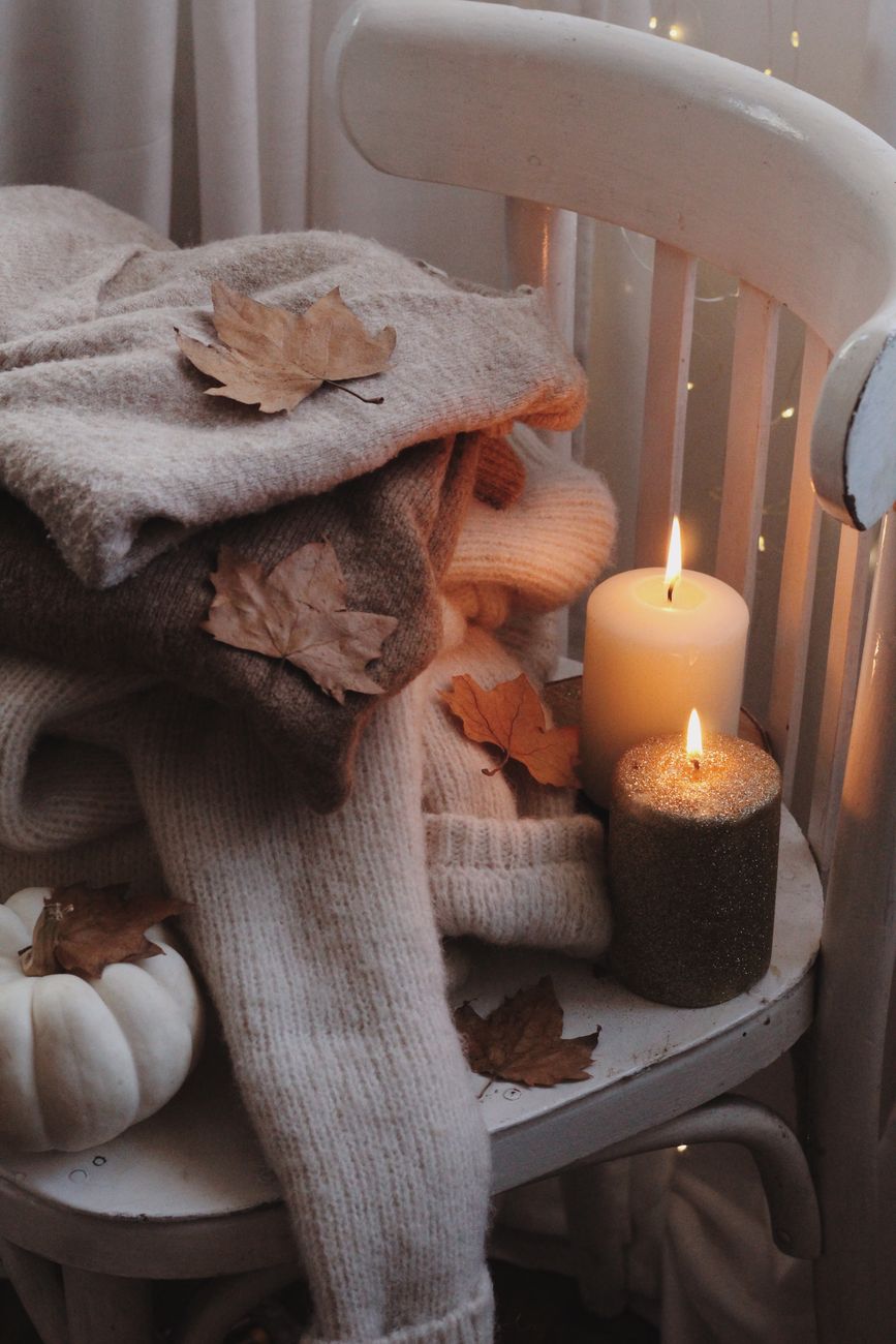 Warm cozy fall setting featuring knitted sweaters, candles, and autumn leaves.