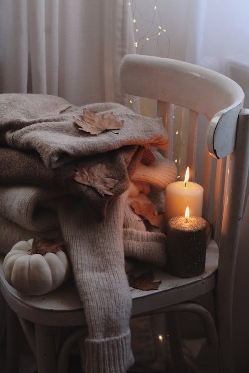 Free Candles on a Chair Beside Knitted Sweaters Stock Photo
