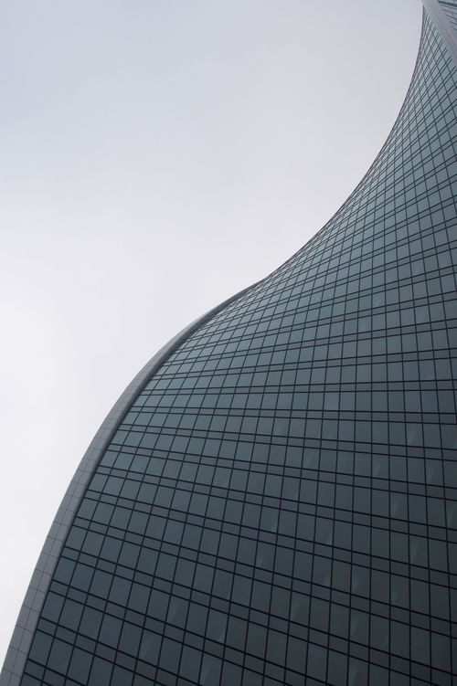 Free Dramatic low angle view of a modern skyscraper with smooth, curved lines against a gray sky. Stock Photo