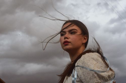 Free Young woman with hair blowing in wind against a moody, cloudy sky. Stock Photo