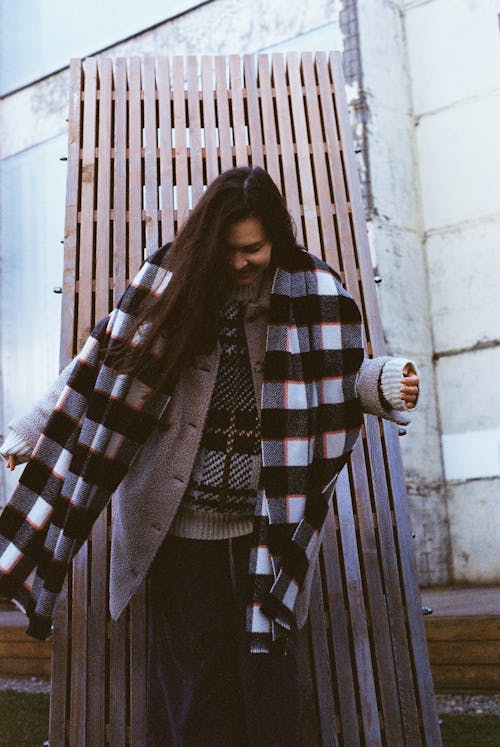 A Woman in Plaid Scarf Standing Near the Wooden Wall
